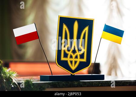 Treffen mit der Ukraine und Polen. Flaggen von Polen und der Ukraine und Dreizack zwischen auf dem Verhandlungstisch. Polen Ukraine Beziehungen Allianz und Handel,trav Stockfoto
