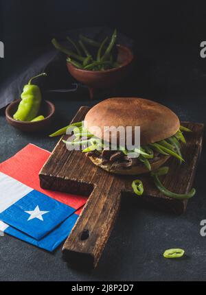 Chilenischer lateinamerikanischer Sandwich-Burger Chacarero mit hochwertigen Rinderschnitten und grünen Bohnen auf schwarzem Hintergrund. Stockfoto