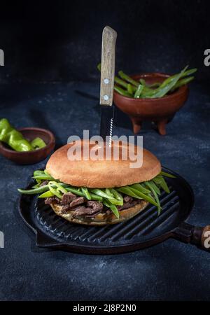 Chilenischer lateinamerikanischer Sandwich-Burger Chacarero mit hochwertigen Rinderschnitten und grünen Bohnen auf schwarzem Hintergrund. Stockfoto