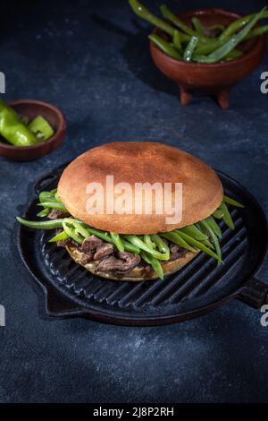 Chilenischer lateinamerikanischer Sandwich-Burger Chacarero mit hochwertigen Rinderschnitten und grünen Bohnen auf schwarzem Hintergrund. Stockfoto