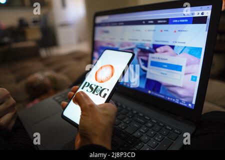 In dieser Abbildung hält eine Hand ein Smartphone mit dem Logo der Public Service Enterprise Group (PSEG), das auf dem Bildschirm angezeigt wird, und die Website der Public Service Enterprise Group (PSEG) im Hintergrund. Stockfoto