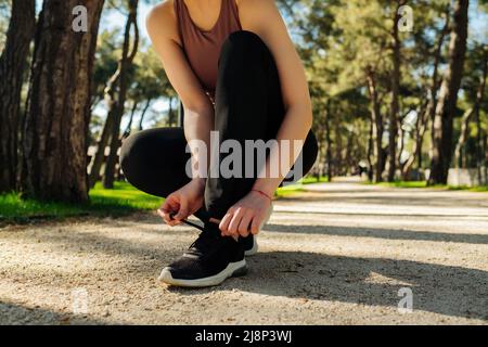 Sportläuferin bereitet sich auf den Weg zum Joggen im Freien vor. Laufschuhe - Nahaufnahme einer Frau, die einen Sport-BH und schwarze Leggings trägt Stockfoto