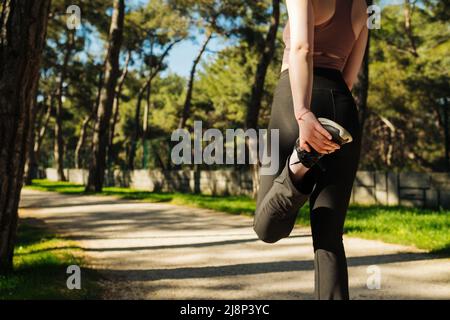 Junge Fitness-Läuferin mit Sport-BH und schwarzen Legging-Stretching-Beinen vor dem Lauf in der Stadt. Urbanes Workout- und Laufkonzept. Frau dehnn Stockfoto