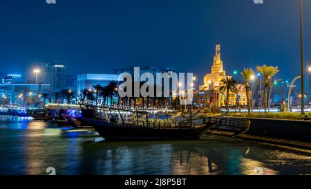 Doha, Katar - 05,2022. Mai: Blick auf die qatar Corniche in der Nacht mit einer bunt dekorierten traditionellen Dhow mit fanar-Gebäude im Hintergrund. Stockfoto