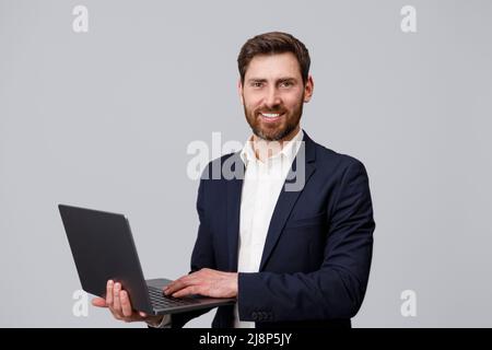 Lächelnder männlicher Business-Coach in Anzug mit Laptop über grauem Studiohintergrund Stockfoto