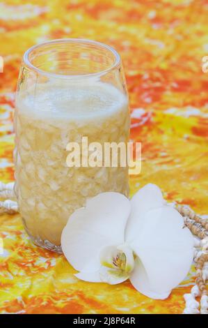 Eiskalt Piña Colada in einem hohen Glas auf festlichem orangefarbenem und gelbem tropischem Drucktuch mit einer einzigen weißen Mottenorchidee. Stockfoto