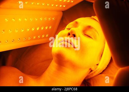 Eine ältere Frau durchläuft eine Gesichtsverjüngung. Frau Gesicht lt Rotlichtbehandlung in der Schönheitsklinik. Kosmetologie. Stockfoto