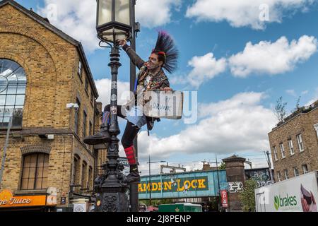 Ein Punk-Rocker mit einer fantastischen Mohawk-Frisur, gespaltener Zunge, Gesichts-Tattoos und Piercings, die in Camden Lock einen Laternenpfosten klettern. Stockfoto