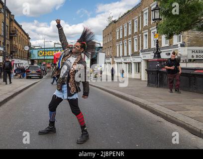 Ein Punk-Rocker mit einer fantastischen Mohawk-Frisur, der mitten auf der Straße steht, eine geballte Faust hebt und durch gerissene Zähne knurrst Stockfoto