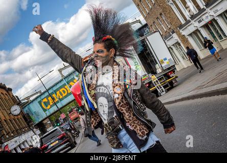 Ein Punk-Rocker mit einer fantastischen Mohawk-Frisur, der eine geballte Faust hebt und durch gerissene Zähne knurbelt, während er mitten auf der Straße steht, Stockfoto