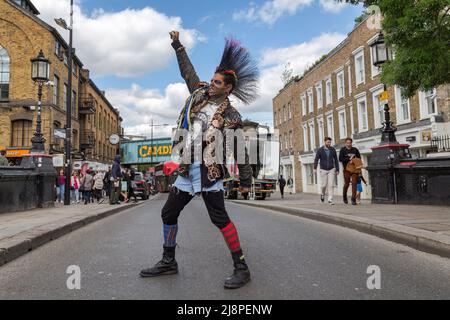 Ein Punk-Rocker mit einer fantastischen Mohawk-Frisur, der mitten auf der Straße steht, eine geballte Faust hebt und durch gerissene Zähne knurrst. Stockfoto