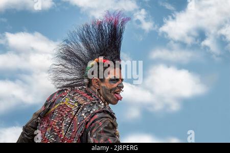 Ein Punk-Rocker mit einer fantastischen Mohawk-Frisur, gespaltener Zunge, Gesichts-Tattoos und Piercings schlägt eine wütende Pose. Stockfoto
