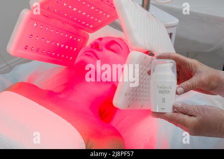 Eine ältere Frau durchläuft eine Gesichtsverjüngung. Frau Gesicht lt Rotlichtbehandlung in der Schönheitsklinik. Kosmetologie. Stockfoto