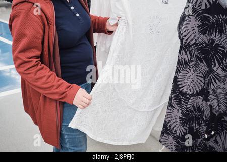 Die Schwangerin im Laden wählt ein lockeres, weißes Kleid mit Spitze und transparentem Kleid Stockfoto