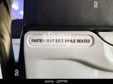 Ein Schild mit der Aufschrift „im Sitzen den Sicherheitsgurt anlegen“ auf einem Flugzeug Stockfoto