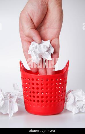 Die Hand legt den Müll in den Korb. Reinigung des Arbeitsplatzes. Ein Mann räumt das Büro auf. Stockfoto