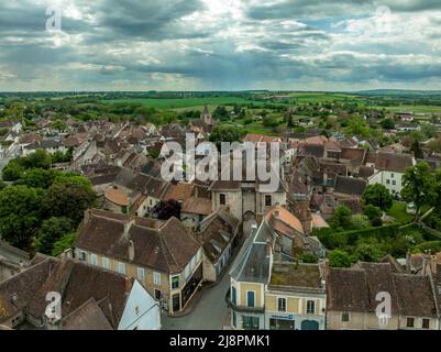 Luftaufnahme von Ainay le Chateau aus dem Osten, kleine mittelalterliche Stadt im Département Allier in Frankreich mit Stadtmauer und Stadttor-Uhrturm bewölktem Himmel Stockfoto