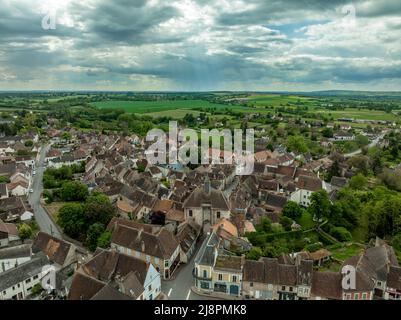 Luftaufnahme von Ainay le Chateau aus dem Osten, kleine mittelalterliche Stadt im Département Allier in Frankreich mit Stadtmauer und Stadttor-Uhrturm bewölktem Himmel Stockfoto