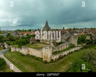 Luftaufnahme von Ainay le Chateau aus dem Osten, kleine mittelalterliche Stadt im Département Allier in Frankreich mit Stadtmauer und Stadttor-Uhrturm bewölktem Himmel Stockfoto