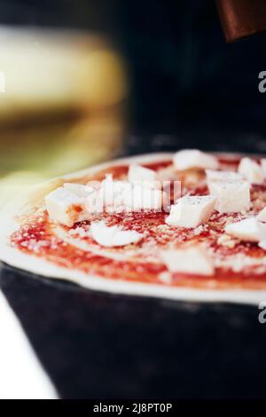 Der Teig und die Toppings sind fertig zum Backen. Der Prozess der Herstellung von hausgemachter Pizza. Das Konzept der hausgemachten Fast Food. Vertikales Foto. Stockfoto