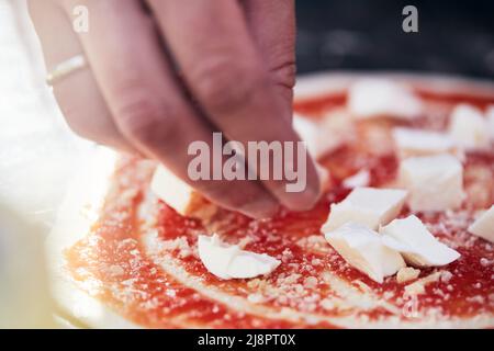 Käse wird mit Sauce auf den Pizzateig gelegt. Der Prozess der Herstellung von hausgemachter Pizza. Das Konzept der hausgemachten Fast Food. Vorderansicht. Stockfoto