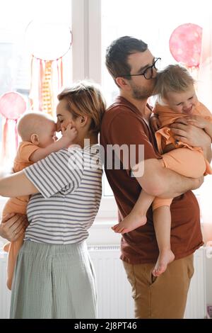 Mutter und Vater umarmten die Kinder zu Hause mit einem Traumfänger-Sonnenfenster. Glückliche Eltern spielen mit Kleinkind, Kleinkind auf Sonnenlicht Stockfoto