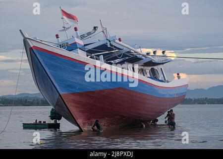 Kendari, Indonesien. 17.. Mai 2022. Fischer reinigen das Boot von Austern, die am Rumpf befestigt sind, bevor sie den Rumpf in Kendari lackieren. Fischer in Kendari nutzen die ungünstige Wetterlage, um zum Meer zu fahren, indem sie ihr Fischerboot reparieren und warten. Kredit: SOPA Images Limited/Alamy Live Nachrichten Stockfoto