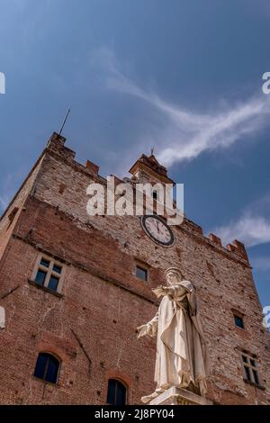 Die antike Statue des Kaufmanns Francesco Datini mit dem Palazzo Pretorio im Hintergrund befindet sich auf der Piazza del Comune in Prato, Italien Stockfoto