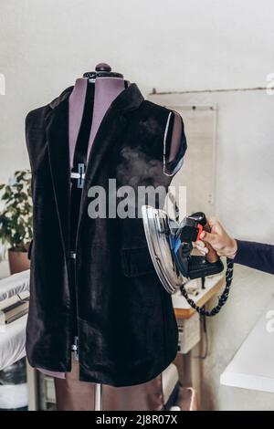 Eine Näherin bügelt eine unvollendete Jacke auf eine Schaufensterpuppe. Stockfoto