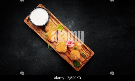 Camembert fries mit Sauce auf einem Holzbrett, auf einem dunklen Hintergrund Stockfoto