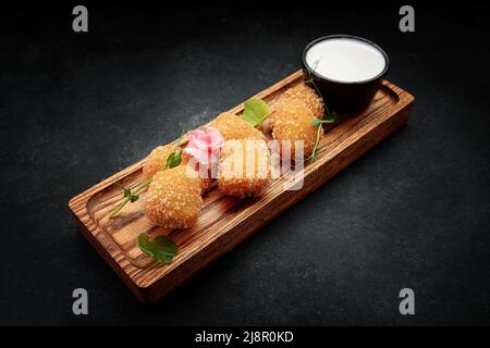 Camembert fries mit Sauce auf einem Holzbrett, auf einem dunklen Hintergrund Stockfoto