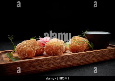 Camembert fries mit Sauce auf einem Holzbrett, auf einem dunklen Hintergrund Stockfoto