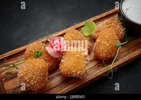 Camembert fries mit Sauce auf einem Holzbrett, auf einem dunklen Hintergrund Stockfoto