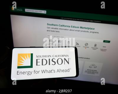 Person, die das Smartphone mit dem Logo des US-amerikanischen Unternehmens Southern California Edison (SCE) auf dem Bildschirm vor der Website hält. Konzentrieren Sie sich auf die Telefonanzeige. Stockfoto