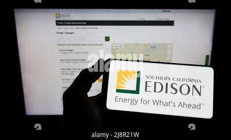 Person mit Mobiltelefon und Logo des US-Unternehmens Southern California Edison (SCE) auf dem Bildschirm vor der Business-Webseite. Konzentrieren Sie sich auf die Telefonanzeige. Stockfoto