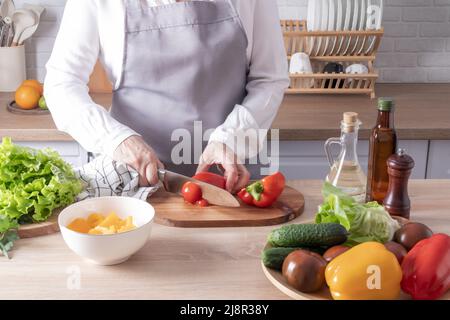 Eine ältere Frau schneidet rote, frische Paprika auf ein Schneidebrett. Nahaufnahme der Küche und Arbeitsplatten mit Gemüse in einer Schüssel Stockfoto