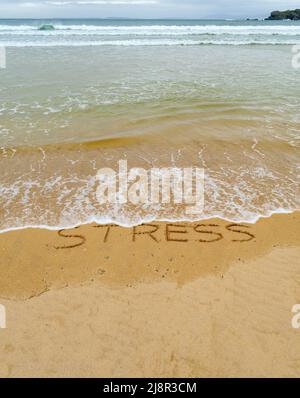 Konzeptbild - um den Stress abzuwaschen, indem man einen Urlaub macht, während die Wellen an einem Sandstrand das Wort „Stress“, das in Sand geschrieben ist, wegspülen. Stockfoto