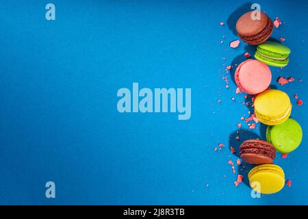 Leuchtend bunte (gelb, rosa, grün, braun) verschiedene Geschmack Macarons süße Kekse auf hohem farbigen Hintergrund. Stapel kleiner französischer Macaronkuchen, Co Stockfoto