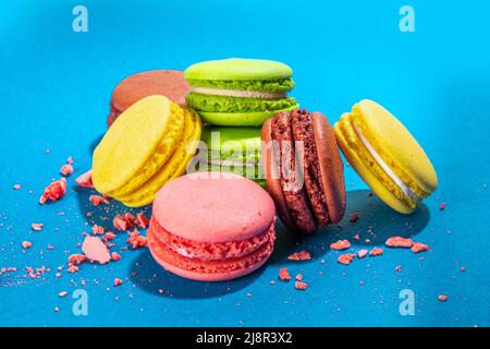 Leuchtend bunte (gelb, rosa, grün, braun) verschiedene Geschmack Macarons süße Kekse auf hohem farbigen Hintergrund. Stapel kleiner französischer Macaronkuchen, Co Stockfoto