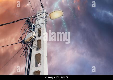 Straßenflutlicht mit vielen Drähten vor dunklem, stürmischen, dramatischen Himmel. Mit Platz für Text. Blackout- und Energiekrisenkonzept Stockfoto