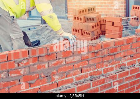 Maurer in Schutzweste und Helm, der mit einer Kelle eine Ziegelwand legt Stockfoto