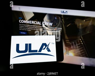 Person mit Mobiltelefon und Logo des amerikanischen Raumfahrtunternehmens United Launch Alliance (ULA) auf dem Bildschirm vor der Webseite. Konzentrieren Sie sich auf die Telefonanzeige. Stockfoto