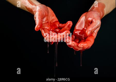 Frauenhände in einer zähflüssigen roten Flüssigkeit ähnlich dem Blut. Stockfoto