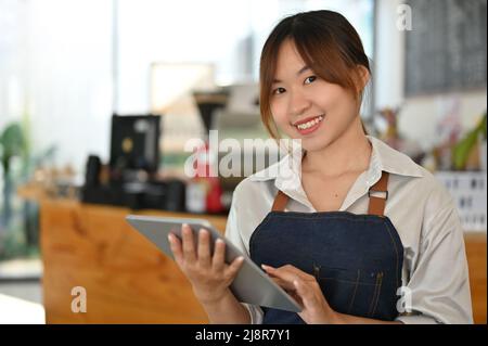 Portrait, ziemlich asiatischer junger Kaffeehaus-Besitzer mit einem digitalen Tablet-Touchpad. Kleinunternehmer. Stockfoto
