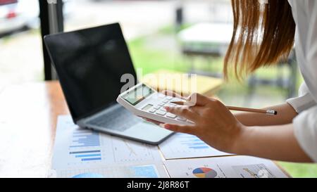 Weibliche Finanzassistentin oder Buchhalterin mit Rechner zur Berechnung einer Umsatz- und Gewinnrechnung auf dem Bericht. Zugeschnittenes Bild Stockfoto
