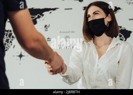 Fröhlicher Touristenmanager, der Happy Client im Büro im Hintergrund der Weltkarte mit der Hand schüttelt Stockfoto