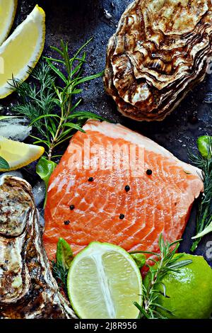 Frisches Fischsteak mit rotem Lachs (Forelle), frischen Austern, Kräutern, Zitrone und Limette. Rohe frische Meeresfrüchte flach, Zitrusfrüchte und Gewürze auf dunklem Hintergrund. Stockfoto