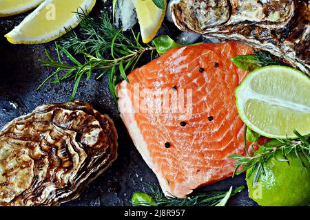Frisches Fischsteak mit rotem Lachs (Forelle), frischen Austern, Kräutern, Zitrone und Limette. Rohe frische Meeresfrüchte flach, Zitrusfrüchte und Gewürze auf dunklem Hintergrund. Stockfoto