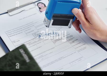 Nahaufnahme einer nicht erkennbaren Person, die als Konsularbeamter in der Botschaft arbeitet, die den Visumantrag genehmigt und das Siegel darauf legt Stockfoto