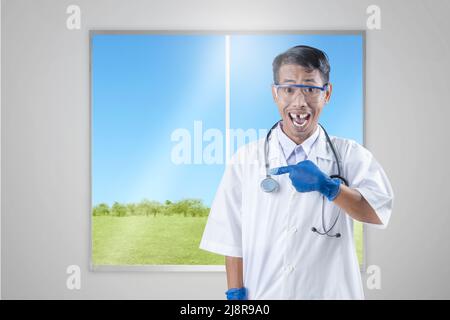 Asiatischer Nerd-Wissenschaftler mit einem Stethoskop, das auf etwas mit Glashintergrund zeigt Stockfoto